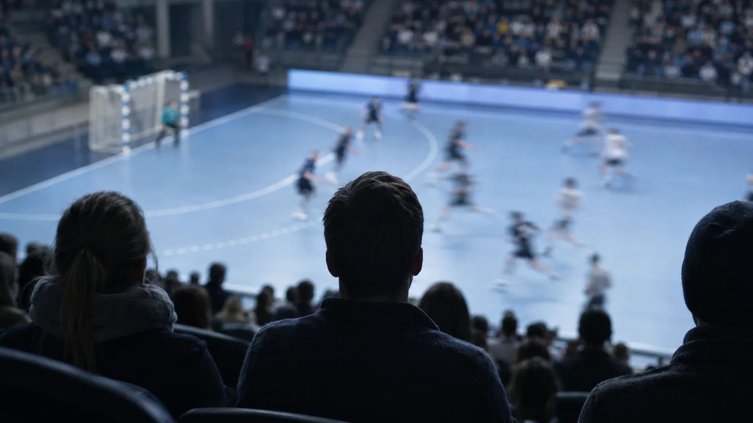 Ishall sedd från läktaren bakifrån, med suddiga spelare på isen långt nere och publik som siluetter under kalla strålkastare.